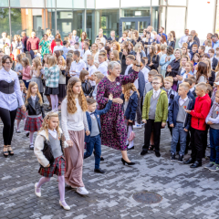 Pirmklasnieki ienāk skolas pagalmā, priekšā klases audzinātāja.