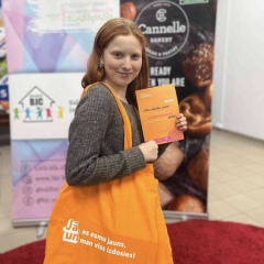 Meitene pie pasākuma reklāmas stenda ar saņemto balvu.