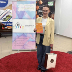 Meitene pie pasākuma reklāmas stenda ar saņemto balvu.