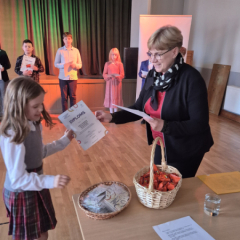 Meitene saņem diplomu no žūrijas pārstāves.