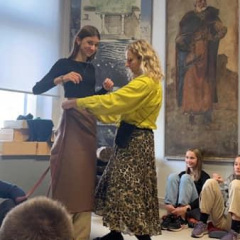 Muzejpedagoģe pielaiko tērpu skolniecei.