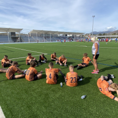 Puiši sēž stadionā, sporta skolotāja motivē puišus spēlei.