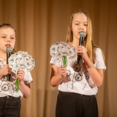 Divas meitenes dzied, rokā mikrofoni un papīra pieneņpūkas.