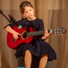 Meitene sēž un  spēlē ģitāru.