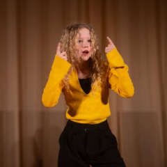 Meitene dzeltenā džemperī dejo.